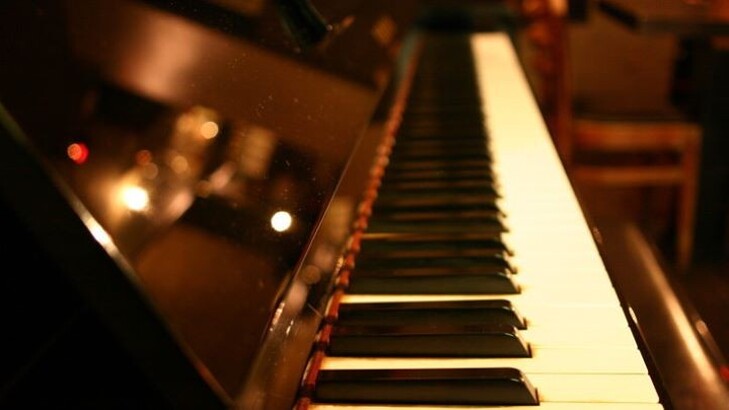 A pianist's hands at a grand piano in the warm low light of Tomi Jazz