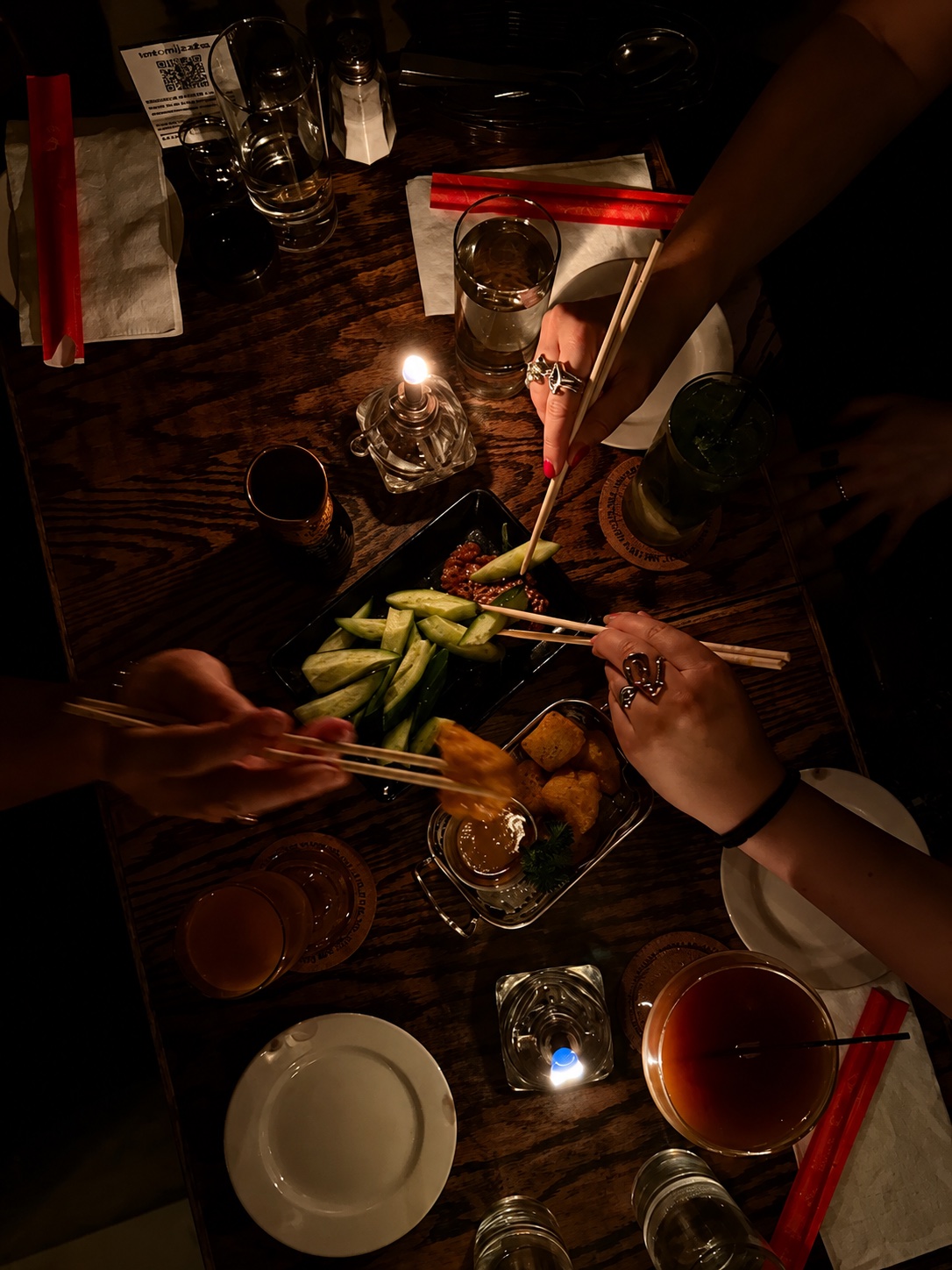 An overhead view of a candlelit table at Tomi Jazz, hands reaching in with chopsticks over shared small plates